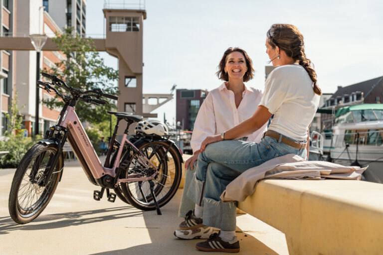 Twee vrouwen op een bank aan het water naast een Granville Suburban en Comfort Ultra e-bike